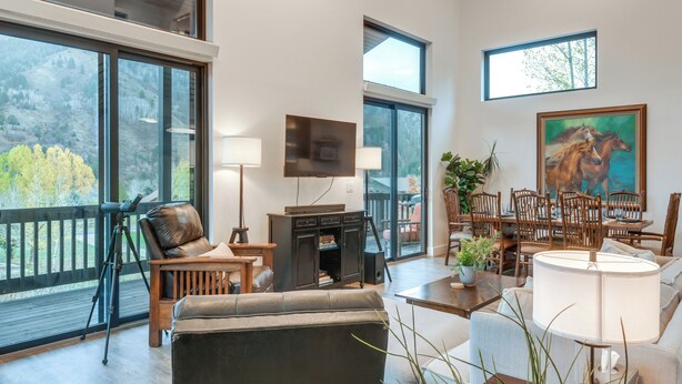 Amplia sala de estar con un ventanal, chimenea y zona de comedor con mobiliario de madera.