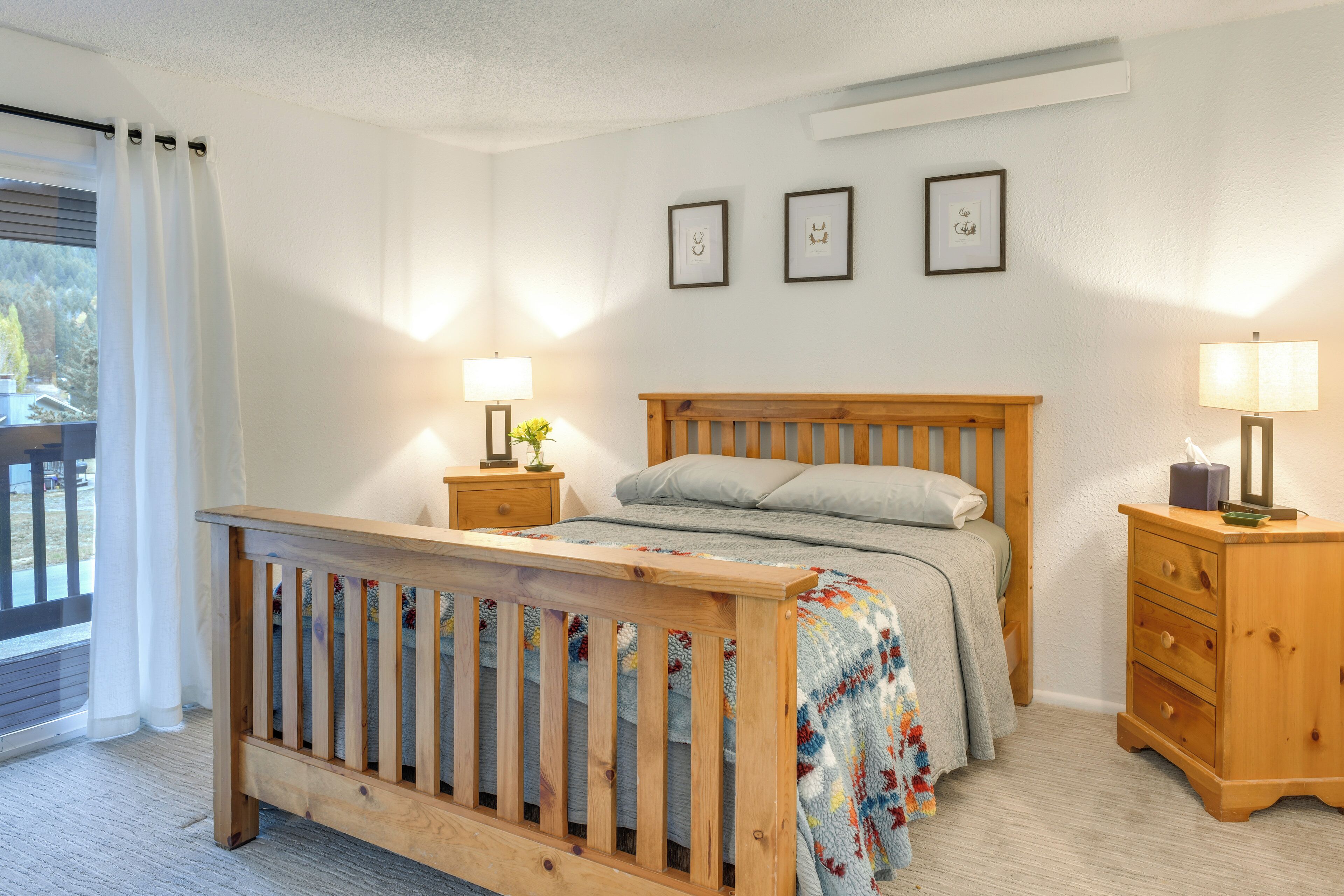 A bedroom with a wooden bed, two bedside tables, a nightstand, and a window with curtains.
