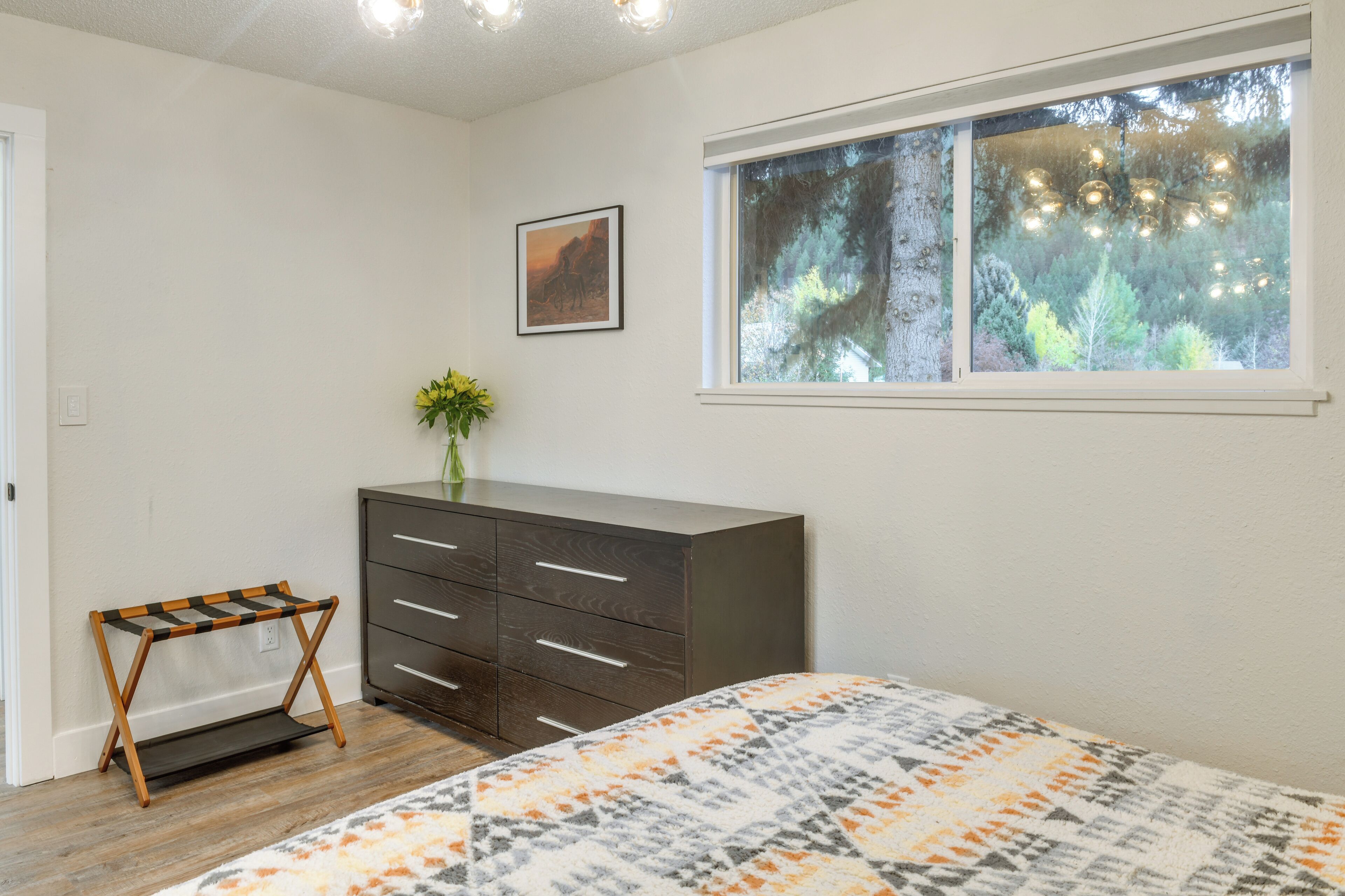 A bedroom with a bed, dresser, and a window with a view of trees.