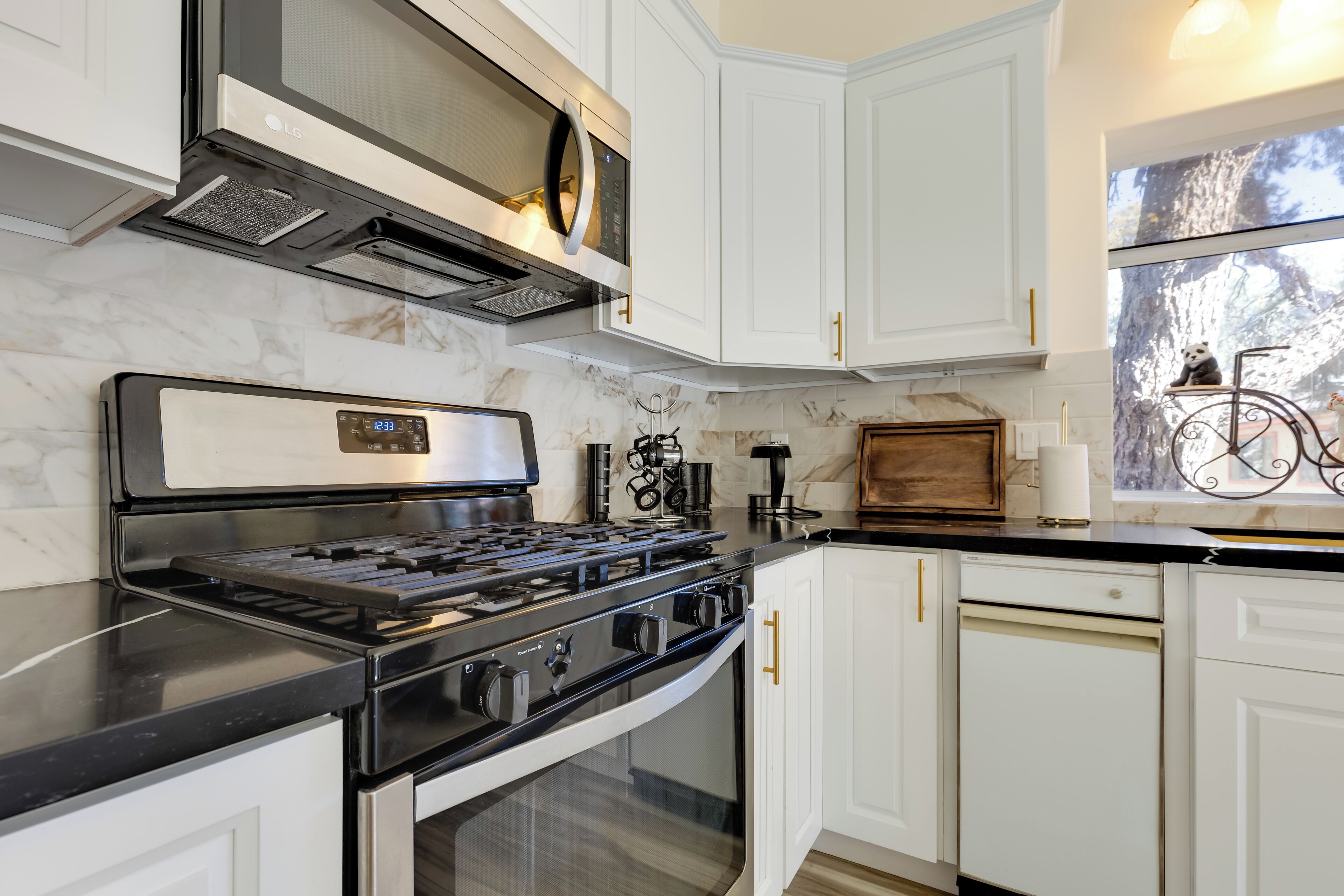 A modern kitchen with white cabinetry, a black countertop, and stainless steel appliances including a stove and oven.