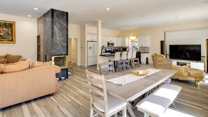 A modern living room with a sofa, dining table, and chairs, a kitchen area with appliances, and a TV. - Game Room & Deck: Modern Frazier Park Home! (Pine Mountain Club)