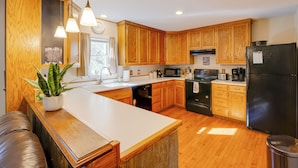 A kitchen with wooden cabinets, a black refrigerator, a microwave, and a sink. - Fish, Hike & Sightsee: Lovely Florissant Cabin! (Florissant)