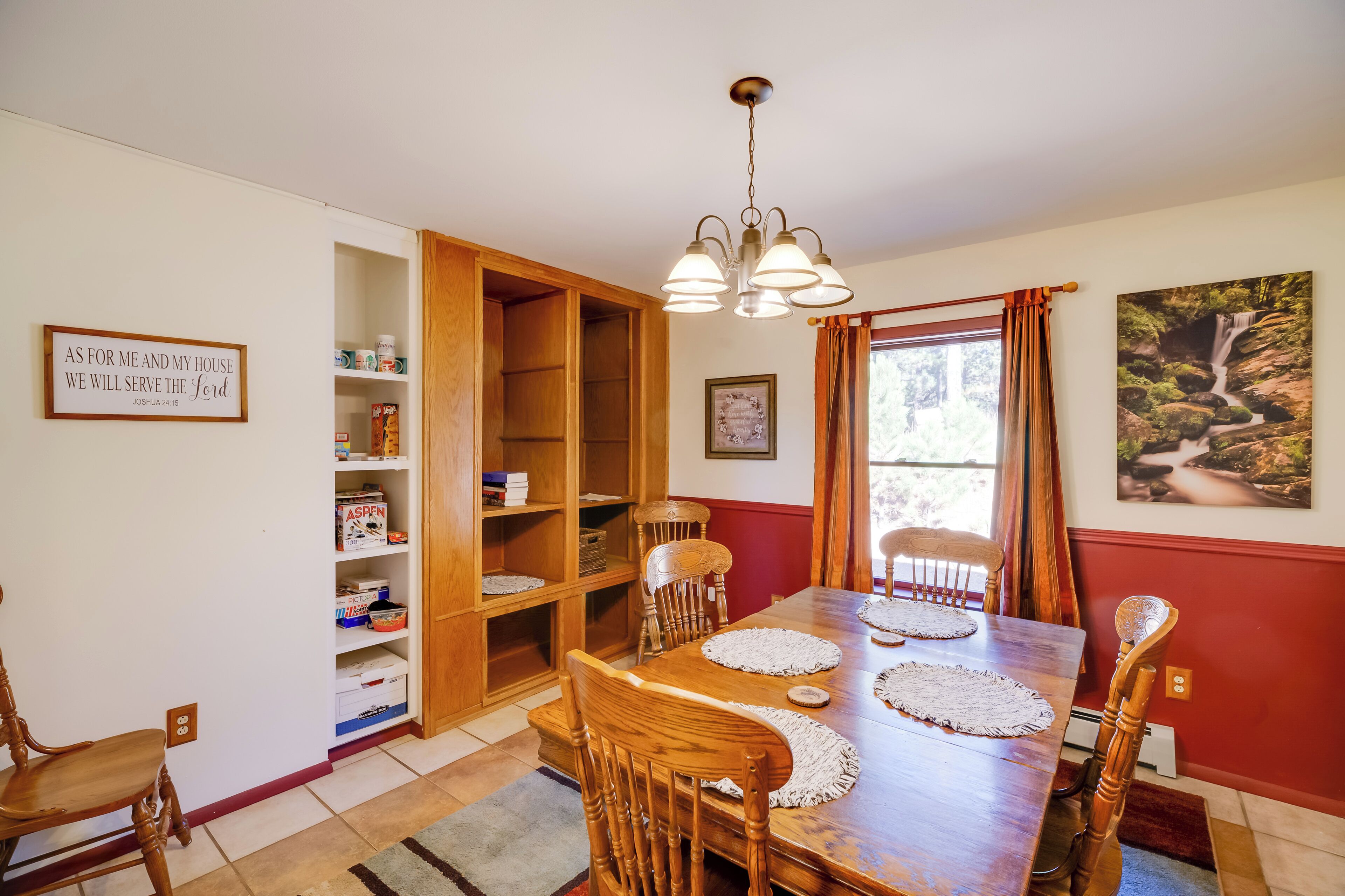 Uma área de refeições com uma mesa de madeira, cadeiras, um lustre e uma estante de livros.