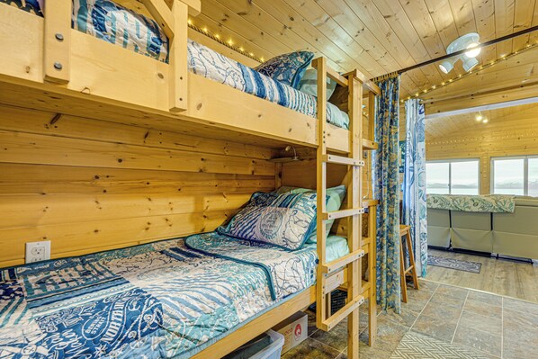 Une chambre avec un lit superposé en bois, une literie à motifs, une petite table et une fenêtre avec des rideaux.