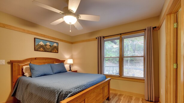 Un dormitorio con una cama de madera, un ventilador de techo, una ventana con cortinas y un cuadro en la pared.