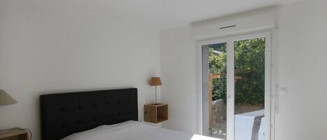A bedroom with a bed, a nightstand, a lamp, and a sliding glass door leading to an outdoor area.
