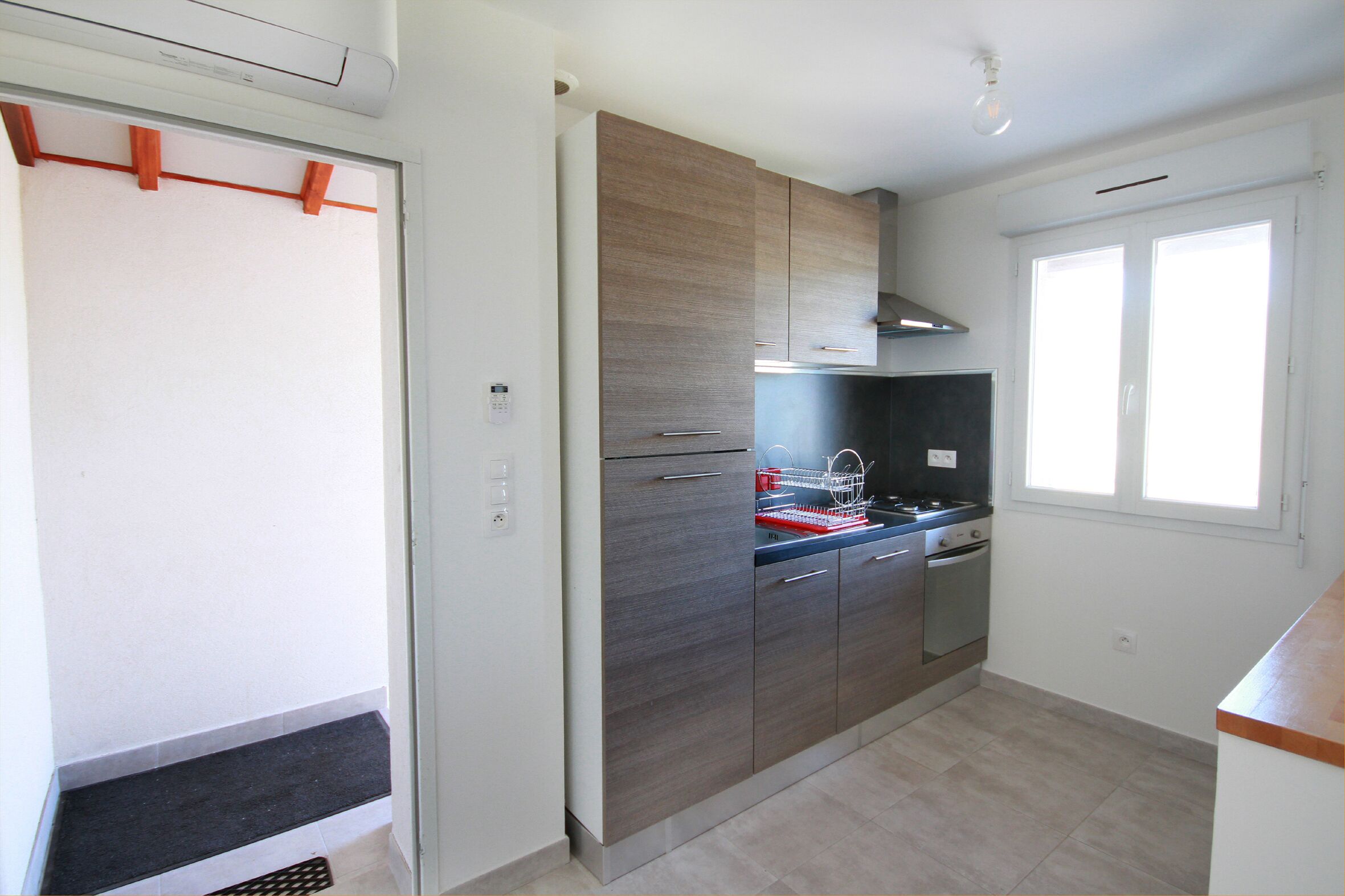 A modern kitchen with grey cabinets, a stainless steel range hood, and a window providing natural light.