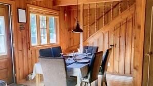 A wooden interior with a dining table set for four, a hanging light fixture, and a staircase leading to an upper level. - Spa & Private Beach | Chalet Natura Versailles (Saint-Côme)