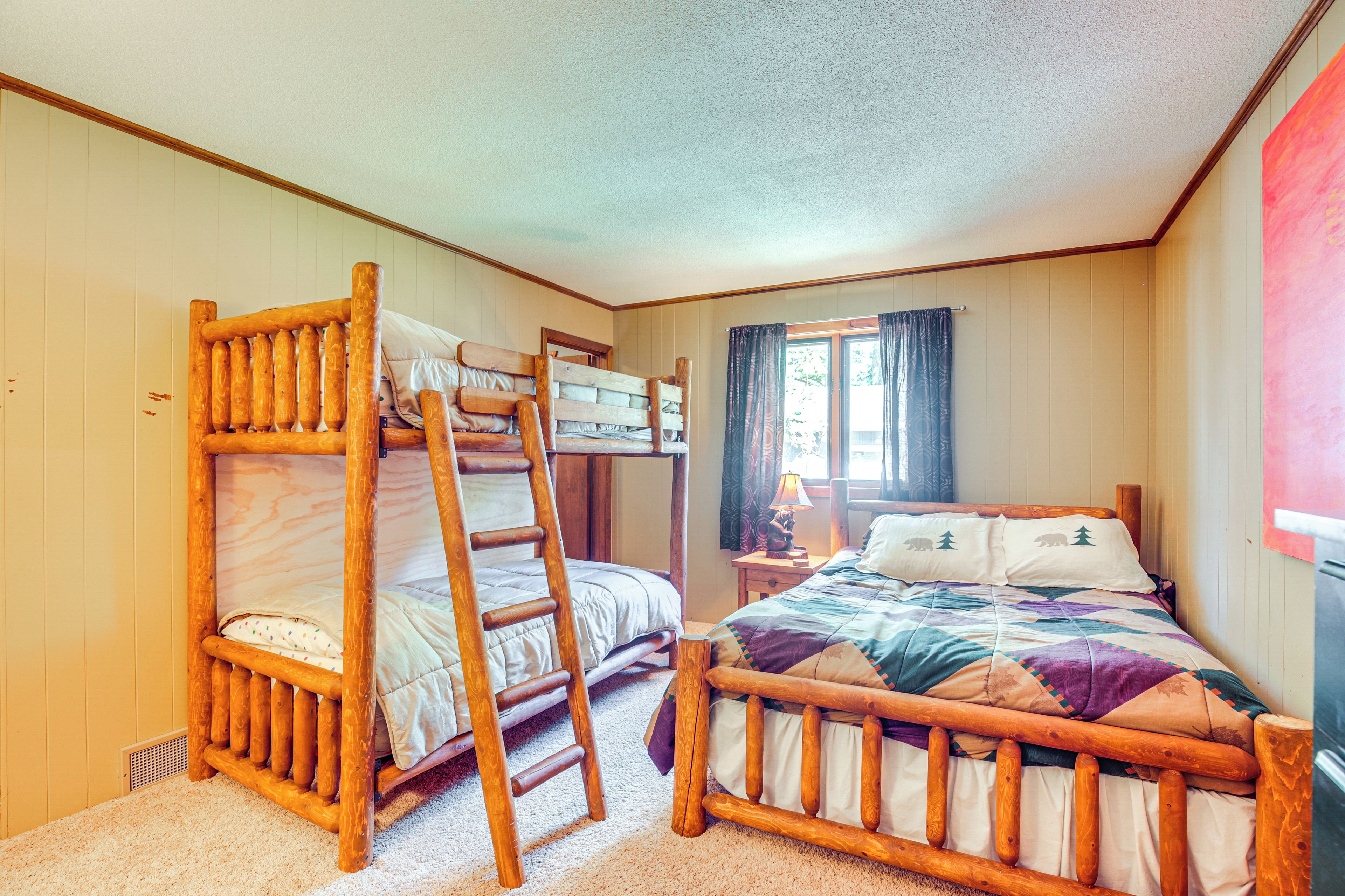 A room with bunk beds, a ladder, a bedside table with a lamp, and a window with curtains.
