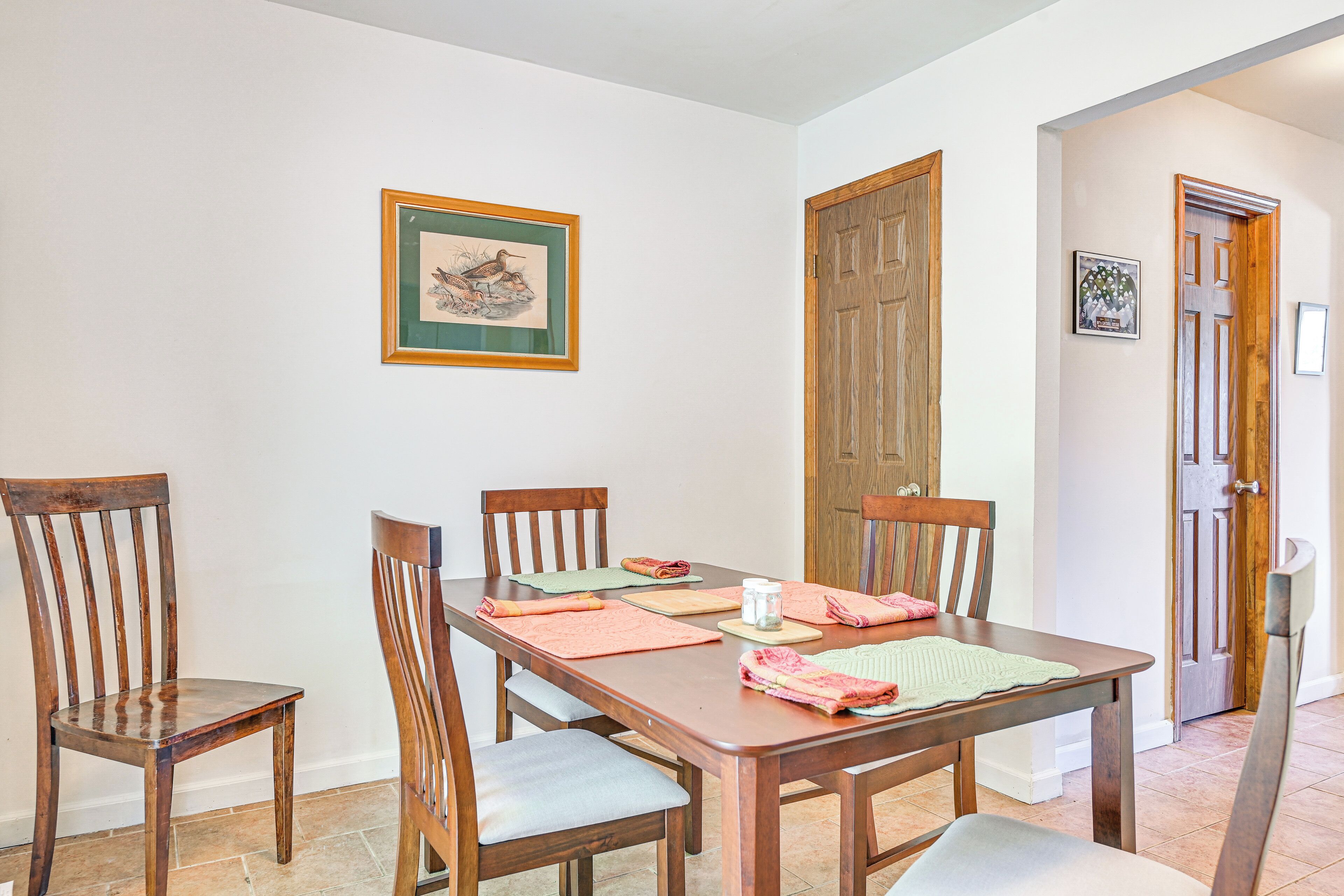 Un coin repas avec une table et des chaises en bois, un tableau encadré au mur et une porte en bois.