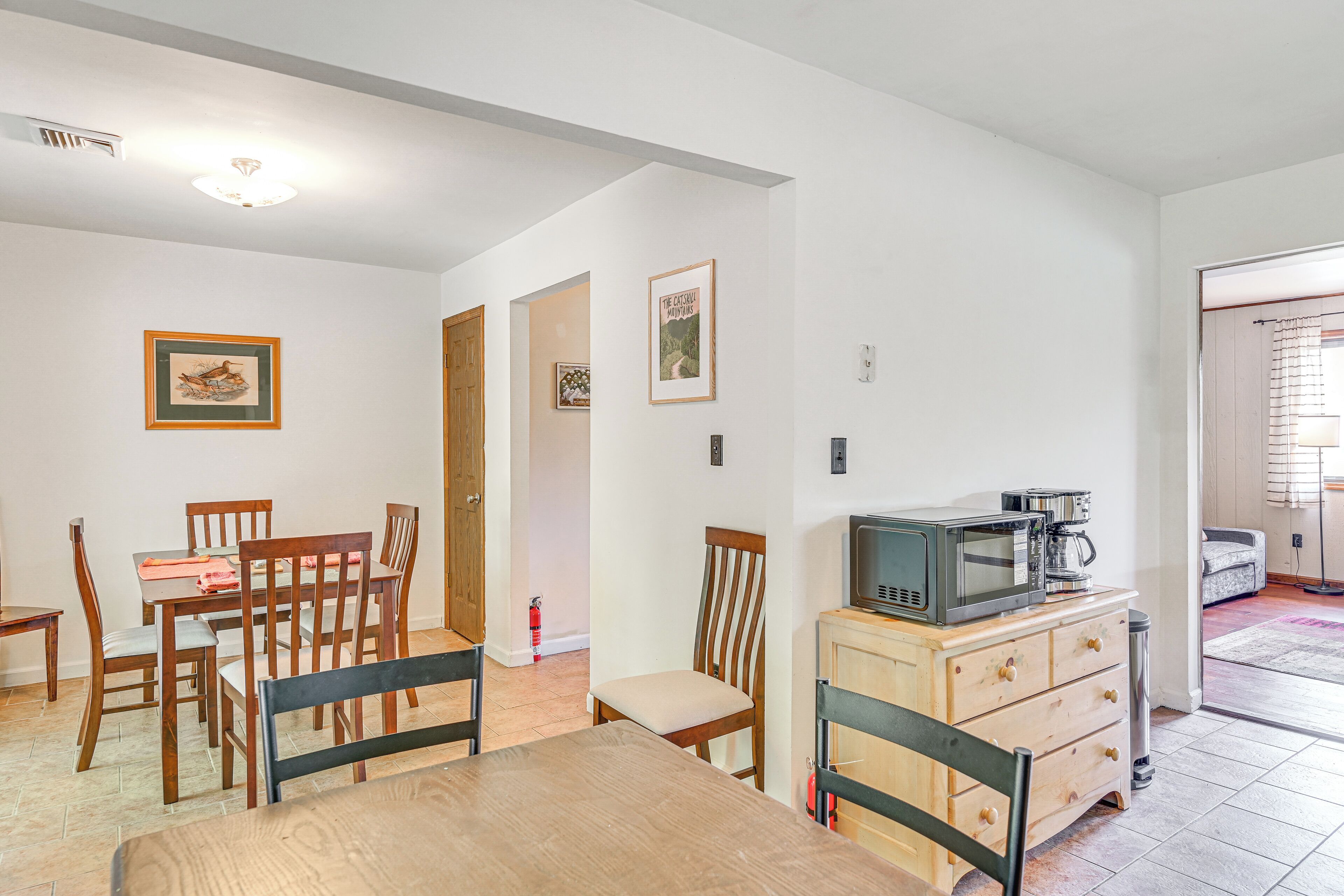 Un comedor con sillas y una mesa de madera, una kitchenette con microondas y una puerta que da a otra habitación.