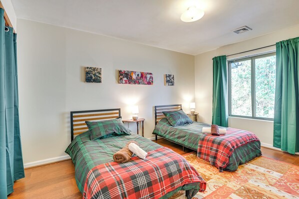 Une chambre avec deux lits, chacun recouvert d’une couverture à carreaux, une petite table de chevet avec une lampe et une fenêtre avec des rideaux.
