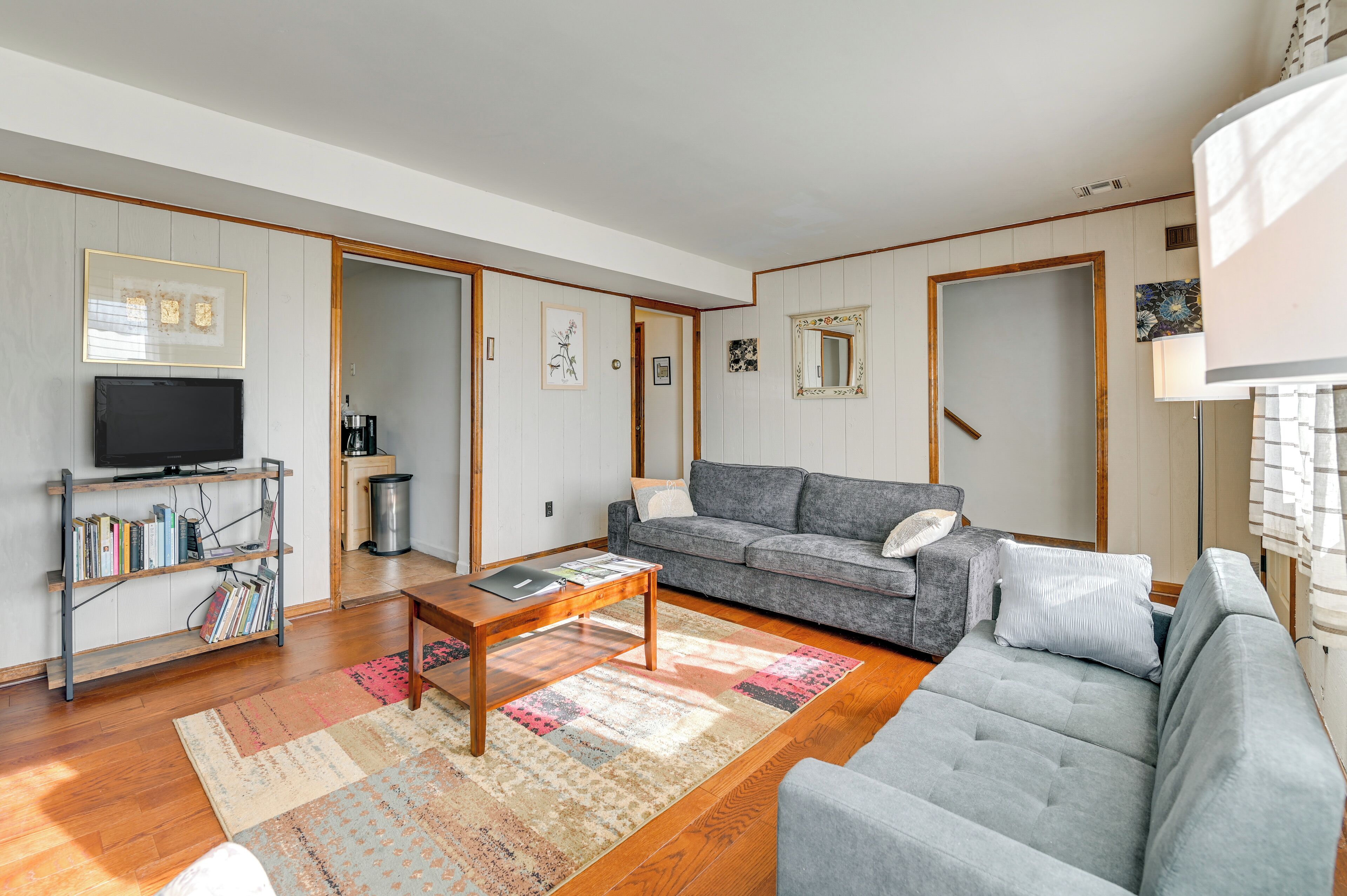 Een moderne woonkamer met een grijze bank, een houten salontafel en een boekenkast met een flatscreen televisie.