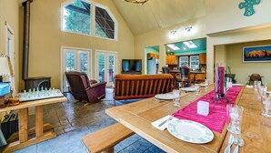 A spacious dining area with a long wooden table set for a meal, a fireplace, and a cozy seating area with a cushioned bench. - Ski, Fish & Explore: Packwood Home w/ Sauna! (Packwood)