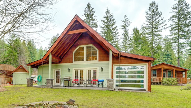 A large, two-story log cabin with a prominent gable roof, a garage, and a fire pit in the front yard. - Ski, Fish & Explore: Packwood Home w/ Sauna! (Packwood)