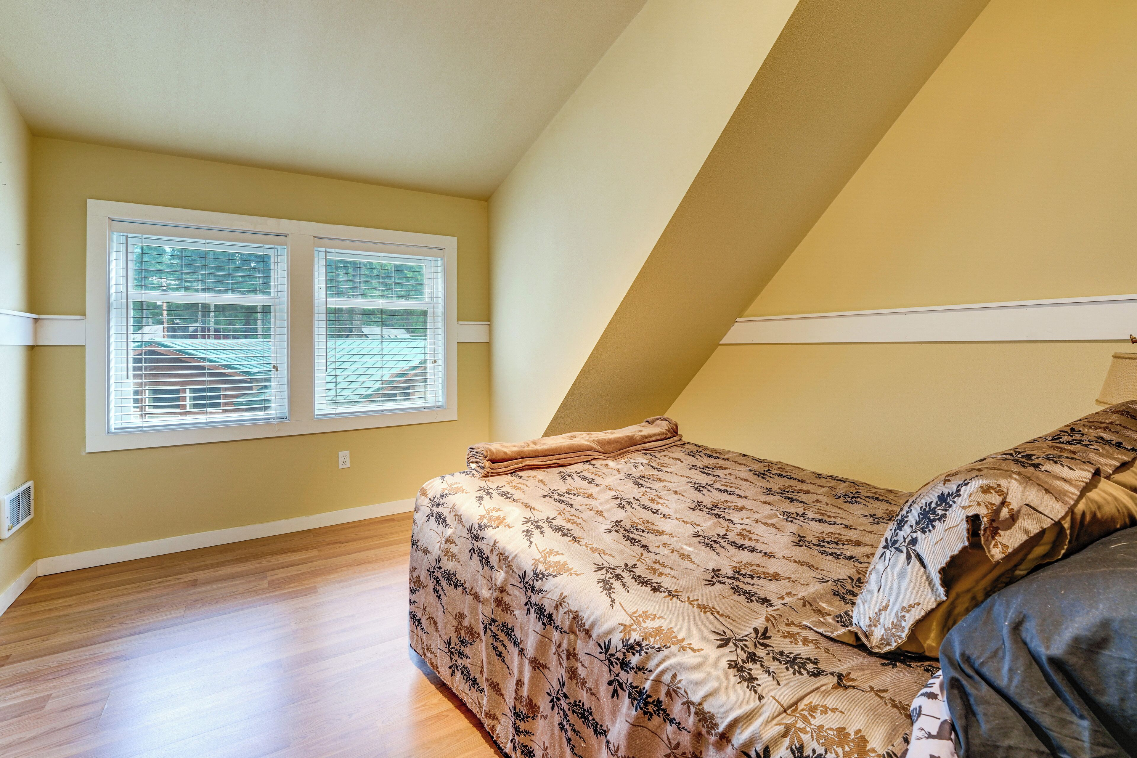 A bedroom with a bed, a window with blinds, and a sloped ceiling.