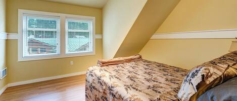 A bedroom with a bed, a window with blinds, and a sloped ceiling.