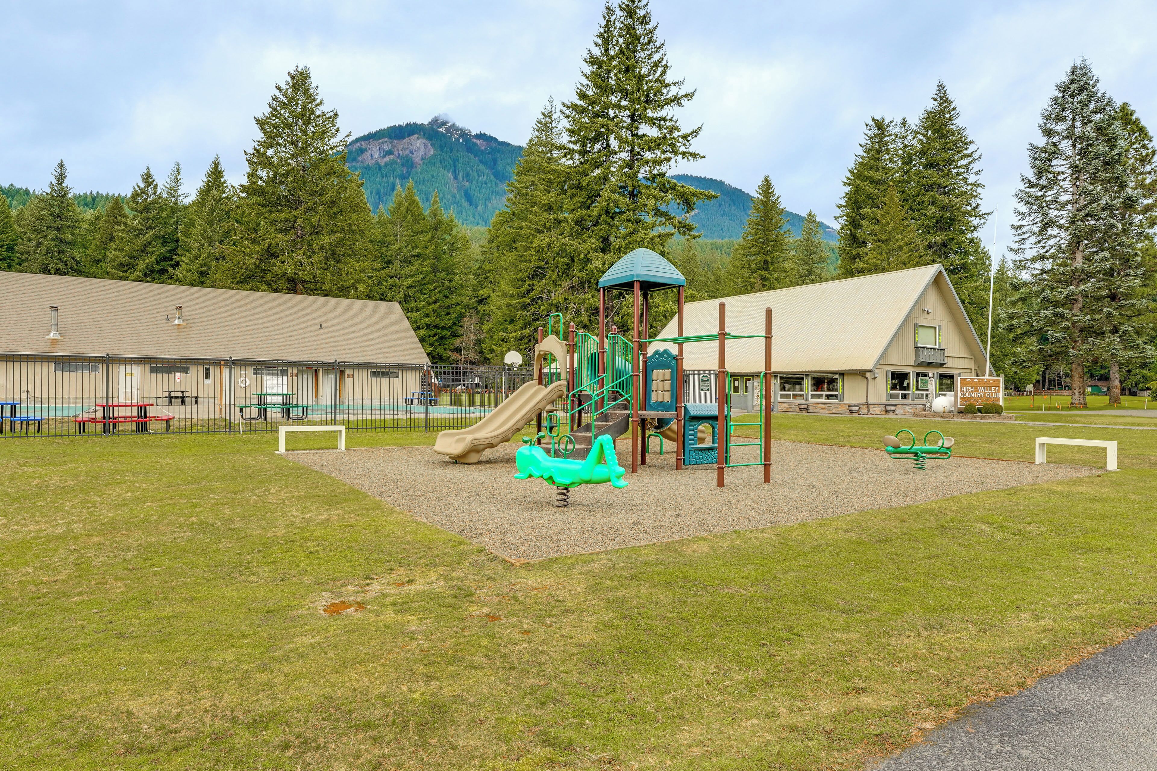 A playground with a slide and climbing structures, surrounded by a fenced area with picnic tables and benches.