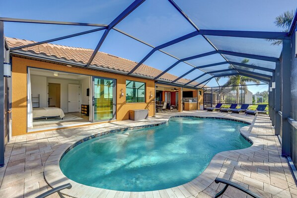 A swimming pool with a curved edge, surrounded by a covered patio area with lounge chairs.