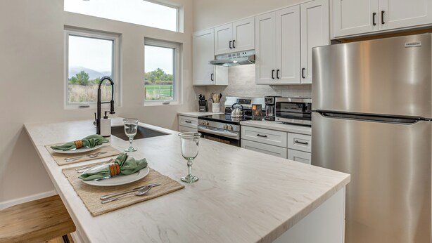 Una cocina moderna con armarios blancos, electrodomésticos de acero inoxidable y una isla grande con encimera de vidrio.