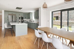 Una cocina moderna con armarios grises, una isla central y un comedor con una mesa de madera larga y sillas blancas.