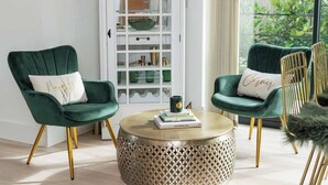 Une pièce comprenant deux fauteuils verts à revêtement en tissu, une table basse ronde et un meuble blanc avec des portes en verre.
