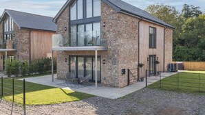Une maison moderne à deux étages, dotée d’une façade en pierre, de grandes fenêtres et d’un patio couvert.