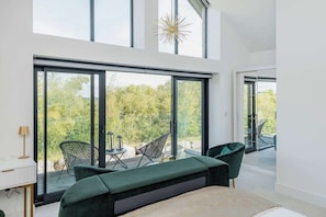 A modern bedroom with large windows, a bed, a desk, and a seating area with chairs. - Gable View (Somerset)