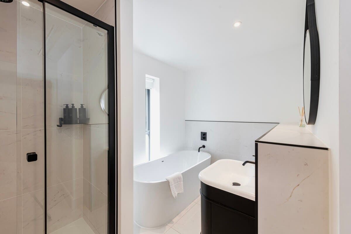 A modern bathroom with a glass shower enclosure, a freestanding bathtub, and a vanity with a mirror.