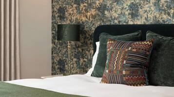 Een net opgemaakt bed met een kussen met een patroon, een lamp en bloemenbehang.