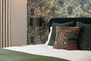 A neatly made bed with a patterned pillow, a lamp, and a floral wallpaper. - Blooms House - Cookswood (Somerset)