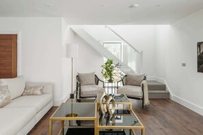A modern living room with a sofa, two armchairs, a coffee table, and a staircase leading to an upper level. - Blooms House - Cookswood (Somerset)