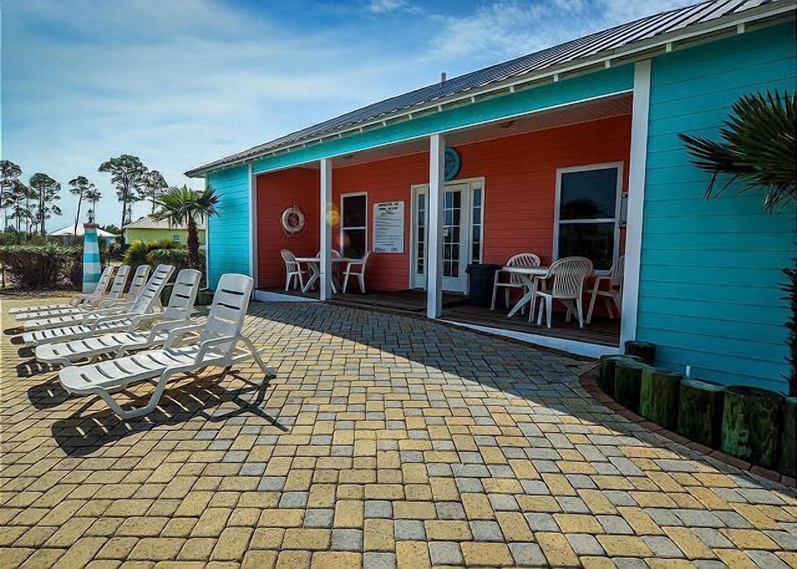 A building with a red and blue exterior, a covered patio with lounge chairs, and a small outdoor seating area.