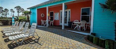 A building with a red and blue exterior, a covered patio with lounge chairs, and a small outdoor seating area.