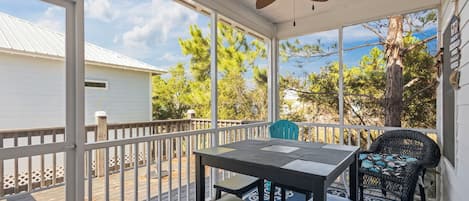 Un espacio al aire libre cubierto con una mesa, sillas, ventilador de techo y vistas a árboles y un edificio.