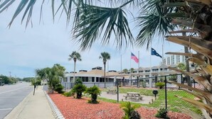 A building with a paved sidewalk, red mulch landscaping, palm trees, and an American flag. - SJ9 Bright studio walk to the beach (Myrtle Beach)