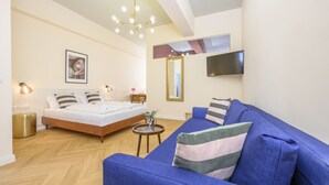 A modern bedroom with a bed, a blue sofa, a TV, and a mirror. - Palais Palffy Hotel Suite in Central Vienna (Vienna)