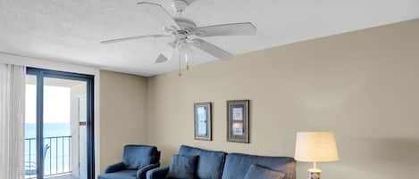 Relax in this stylish living room with a sofa set, coffee table, and side table, plus a ceiling fan and sliding glass door leading to a balcony.