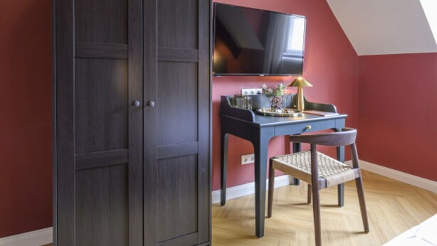 A room with a sloped ceiling, a dark wardrobe, a desk with a chair, a television, and a bed. - Palais Palffy I Suite in Center (Vienna)