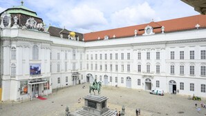 Un edificio grande e histórico con un patio central, una estatua y una alfombra roja que conduce a la entrada.