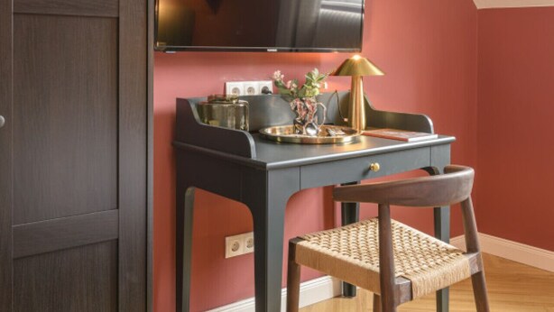Una habitación con un escritorio de madera oscura, una silla, un televisor montado en la pared y una pared decorada en rojo.