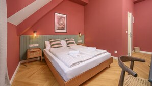 Un dormitorio con techo inclinado, una cama con ropa de cama a rayas, dos mesitas de noche con lámparas y un cuadro en la pared.