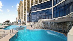 A swimming pool with a waterfall feature, surrounded by a multi-story building with balconies.