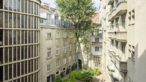 A narrow urban courtyard with buildings on either side, featuring balconies and a central tree.