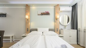 A hotel room with a double bed, two bedside tables, a chair, a desk, a mirror, and an air conditioning unit.