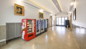 A hallway with vending machines, framed portraits on the walls, and a radiator.