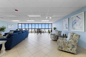Una habitación amplia con un gran ventanal, un sofá azul, un sillón estampado y un comedor con sillas y una mesa.