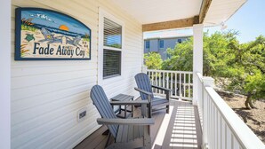 A porch with Adirondack chairs, a table, and a sign reading 'Fade Away Cay'. - Oceanside Duck Retreat w Pool, Spa, Mins to Beach! (Duck)