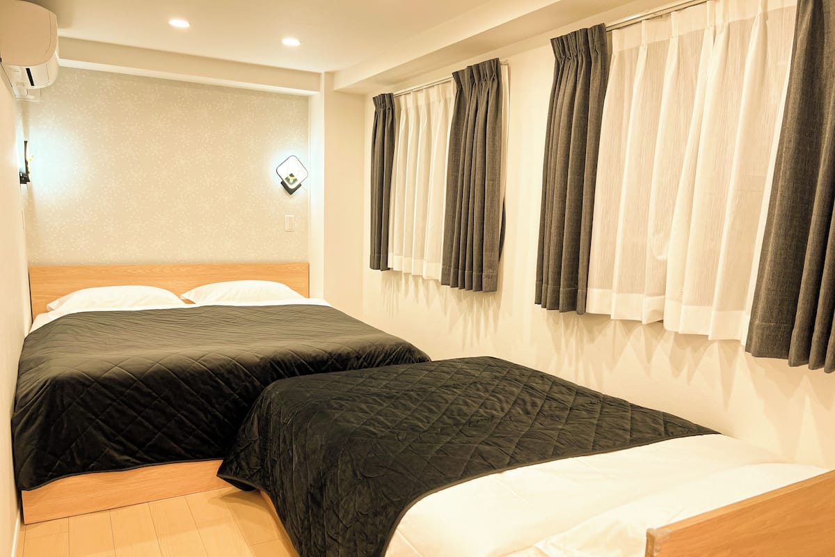 Une chambre d’hôtel avec deux lits, une tête de lit en bois, un climatiseur fixé au mur et une fenêtre avec des rideaux.