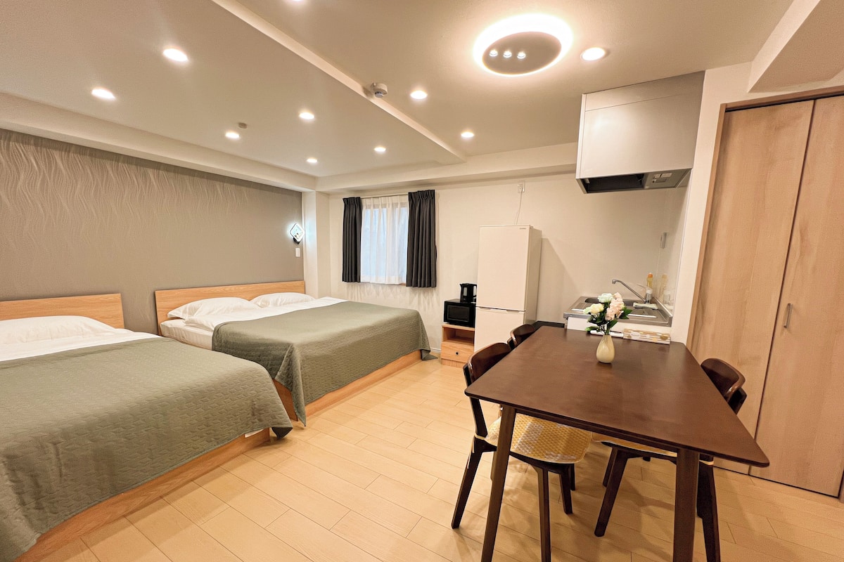 Une chambre d’hôtel avec deux lits, une table à manger, un coin cuisine et une armoire en bois.